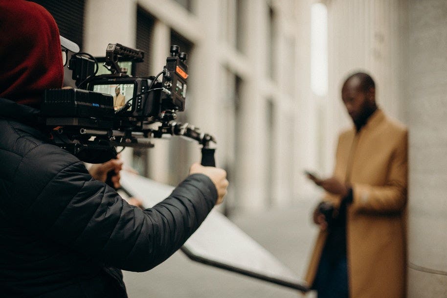 A camera operator holding a gimbal recording a male model in a yellow coat