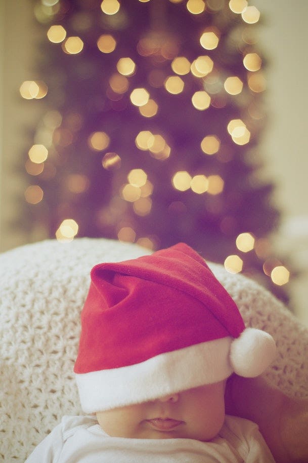 A baby wearing a Santa hat with a Christmas tree in the background