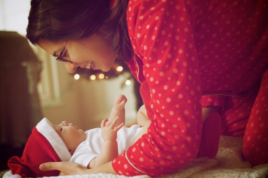 A mum leaning over a baby wearing a Christmas hat.