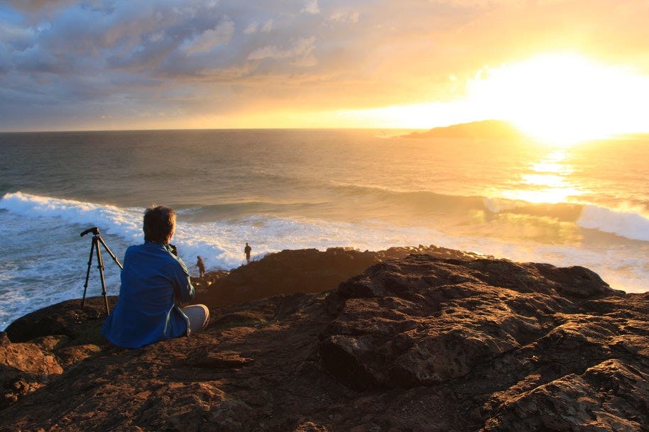 photographer sitting beside tripod watching sunset