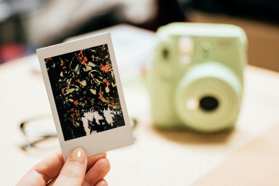 A person holding an instant photo in front of an Instax Mini.