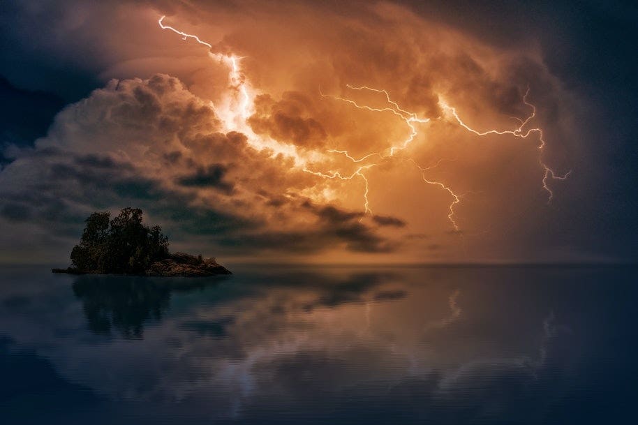 Lightning and storm clouds over a rocky island surrounded by water.