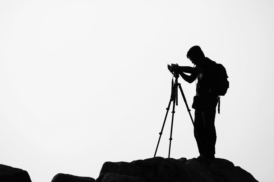 A photographer working on a camera on a tripod over rocky ground.