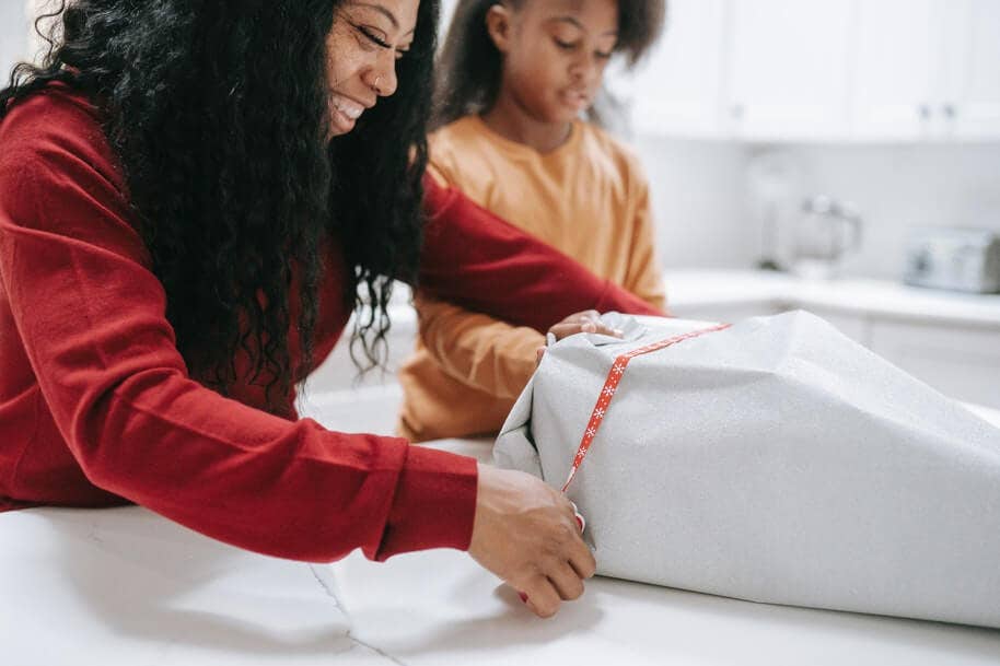 A mother wrapping a Christmas present with her child.