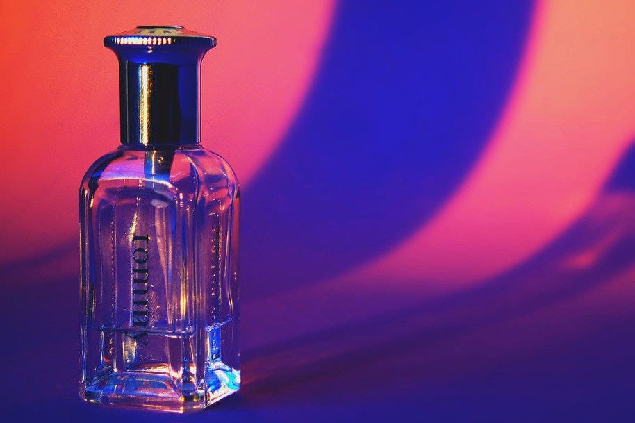 A Tommy perfume bottle that is almost empty against a violet backgrop.