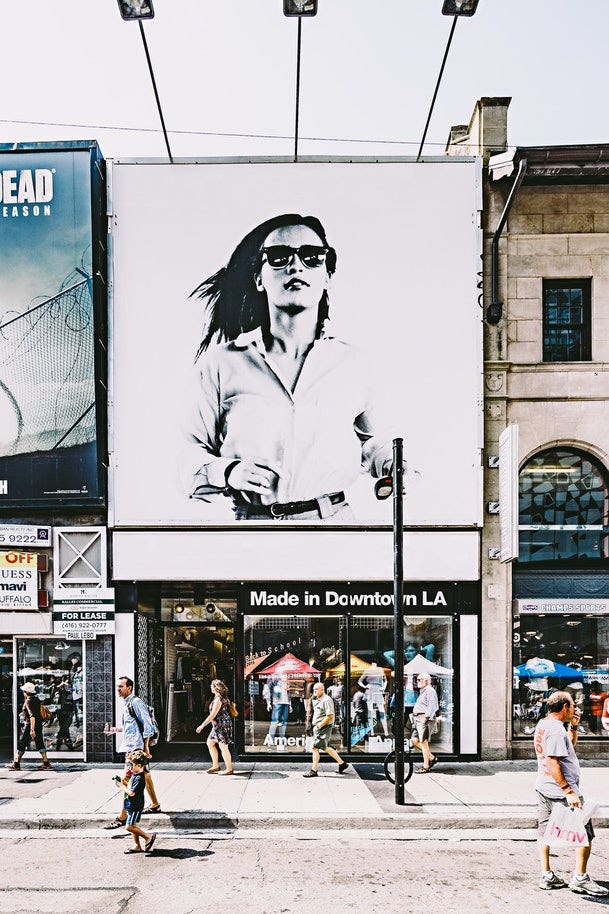 A black and white billboard over a shopfront, depicting a woman running