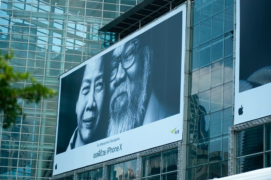 A billboard with two elderly Asian faces smiling with writing underneath advertising the iPhone X