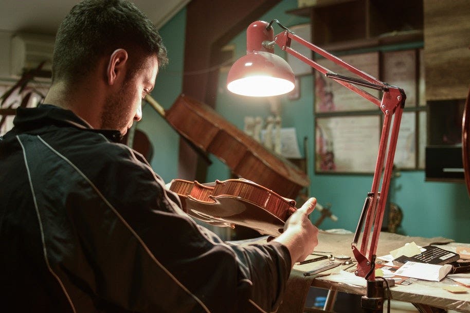 A man studying a violin under a lamp light